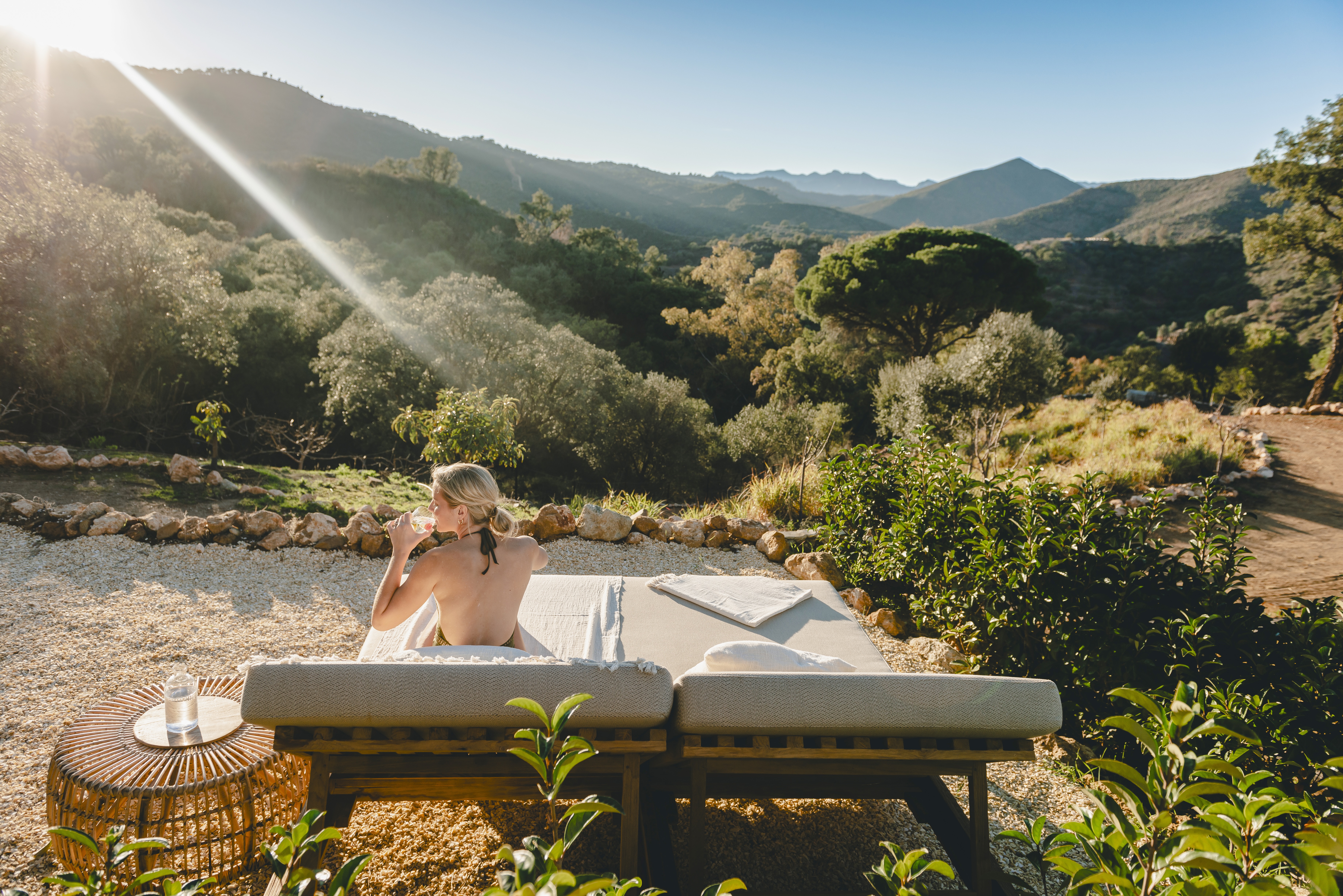 Woman on sunbed looking out over mountain valley in late afternoon light